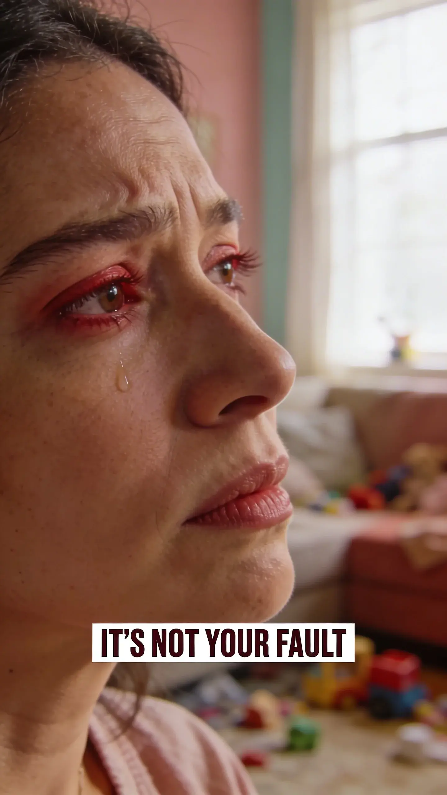 CLOSE-UP FACE EMOTION: close-up face emotion, BASE: vertical 9:16, ultra-tall composition optimized for mobile Pinterest feed, SCENE: An extreme close-up of a mother's face, her eyes slightly red-rimmed and looking away, jaw clenched, a single tear threatening to fall from her lower eyelid. Her brow is deeply furrowed with worry and exhaustion, but there's a subtle flicker of determination in her expression. The background is softly blurred, showing a hint of a messy living room with scattered toys, indicating the overwhelming source of her stress. Her face is raw and authentic, showing the emotional toll of constant demands and the feeling of burnout. , EMOTION HOOK: overwhelmed mom burnout, TOPIC PHRASE: preschooler routine help, TEXT POSITION: BOTTOM-CENTER, OVERLAY: text says exactly: "IT'S NOT YOUR FAULT", bold sans-serif font, high contrast white text with dark outline or shadow so it is readable on mobile, overlay text should be a punchy version of the TOPIC PHRASE or EMOTION HOOK, LIGHT: Soft, diffused natural light from a window, MOOD: overwhelmed, exhausted, guilty, determined, raw, vulnerable, COLOR: muted warm palette (dusty rose, cream, terracotta, soft sage, warm beige), gentle film grain, no logos, no watermarks, QUALITY: photorealistic, 8K, shallow depth of field, film aesthetic, cinematic color grade, no logos, no watermarks